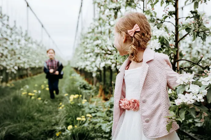 Broer en zus poseren samen voor communiefoto’s in bloesemtuin