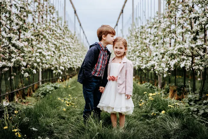 Meisje in communiekleed poseert met broer onder bloeiende takken