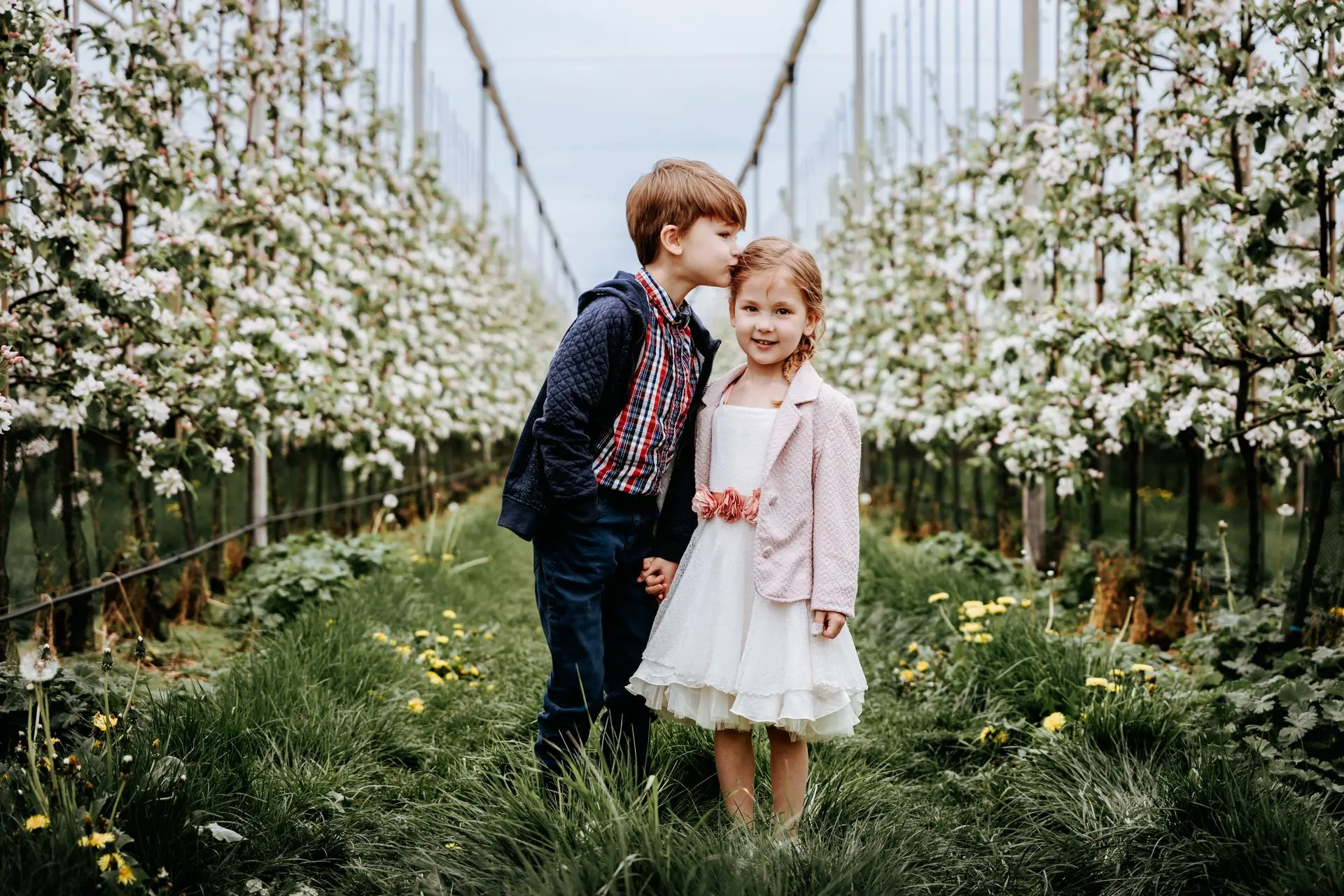 Meisje in communiekleed poseert met broer onder bloeiende takken