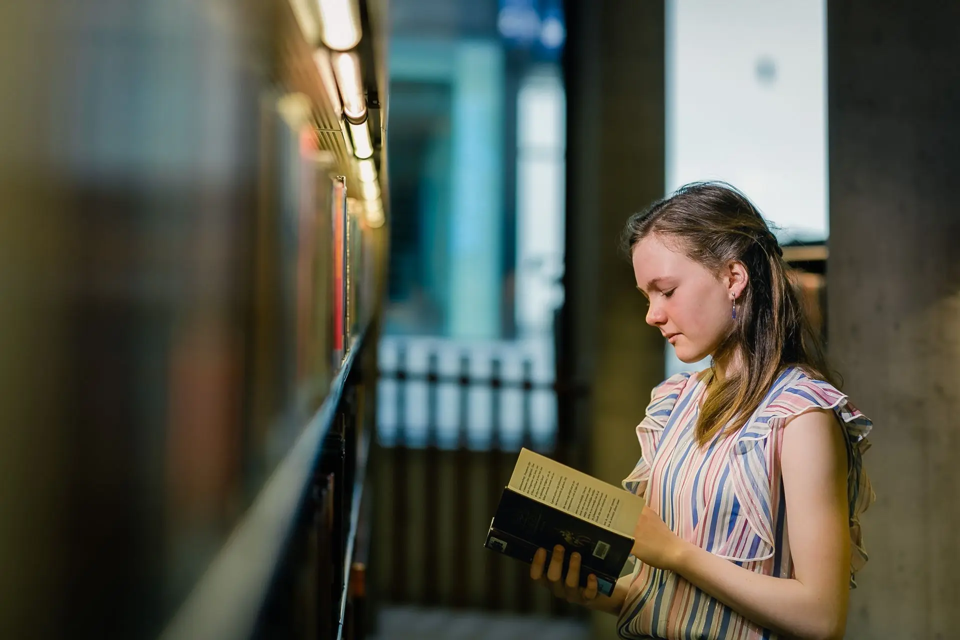 ommunicant poseert tussen boeken in bibliotheek Waregem – stijlvolle communiefoto