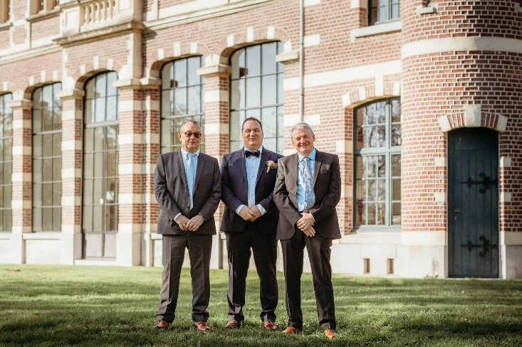 drie mannen in de domein De Ghellinck staan in gras voor het gebouw 