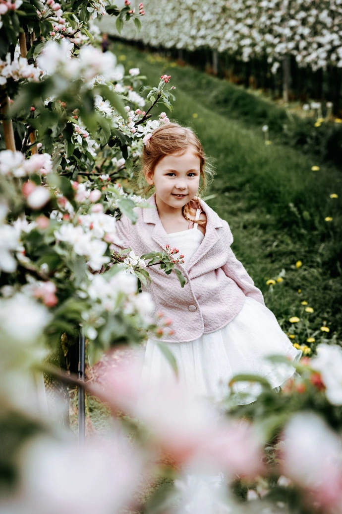 Communiefoto van meisje in pasteljurk tussen bloeiende bloemen