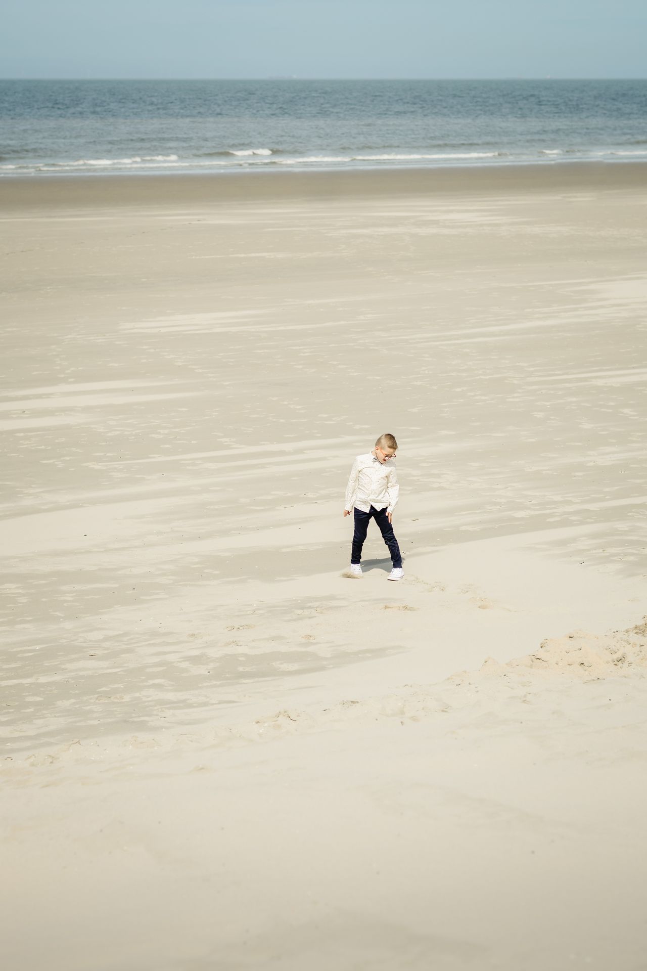 Romantische lentefeestshoot op het strand van Bredene, jongen in chic kostuum met zonlicht en natuur.