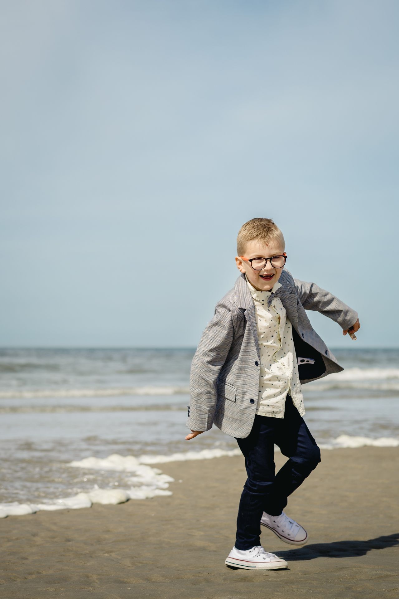 Fotoshoot voor lentefeest aan zee met stijlvolle outfit, duinen en bomen in zonnige setting.