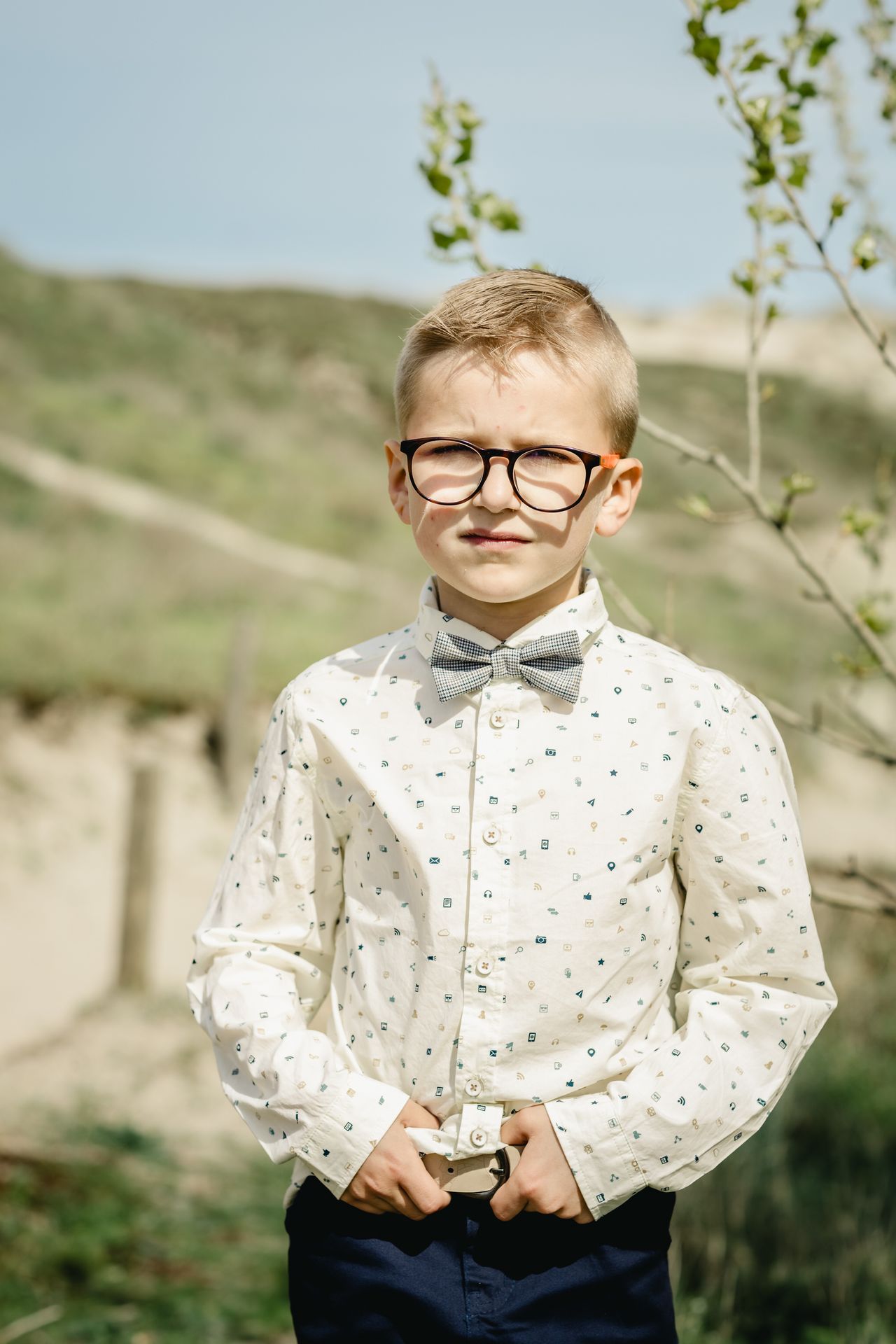 Fotoshoot voor lentefeest aan zee met stijlvolle outfit, duinen en bomen in zonnige setting.