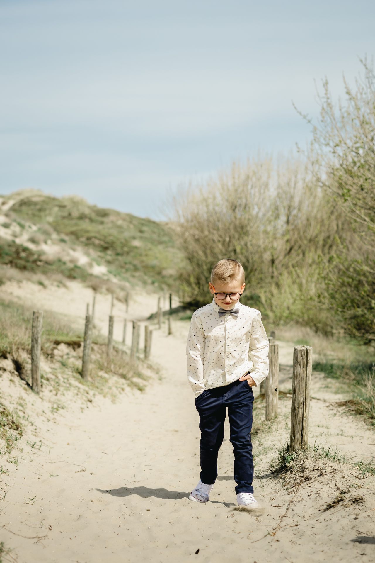 Fotoshoot voor lentefeest aan zee met stijlvolle outfit, duinen en bomen in zonnige setting.