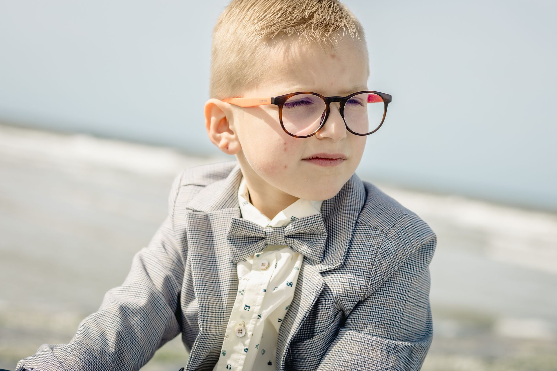 Romantische lentefeestshoot op het strand van Bredene, jongen in chic kostuum met zonlicht en natuur.