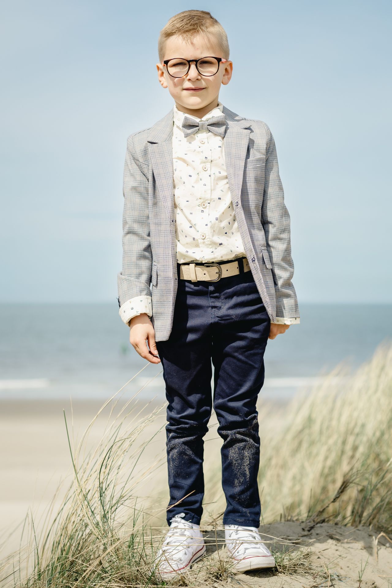 Romantische lentefeestshoot op het strand van Bredene, jongen in chic kostuum met zonlicht en natuur.