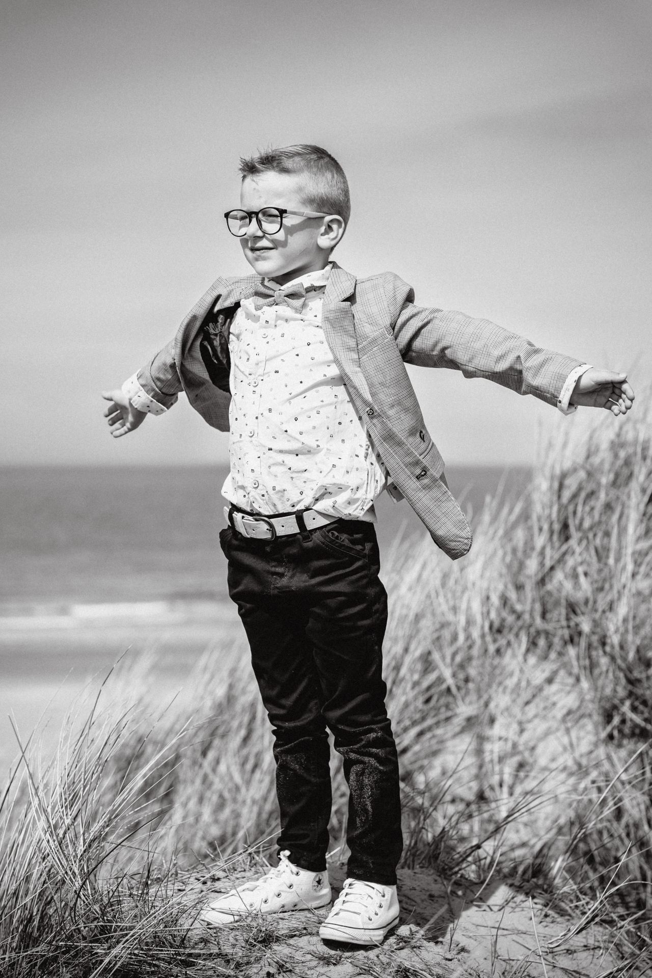 Fotoshoot voor lentefeest aan zee met stijlvolle outfit, duinen en bomen in zonnige setting.