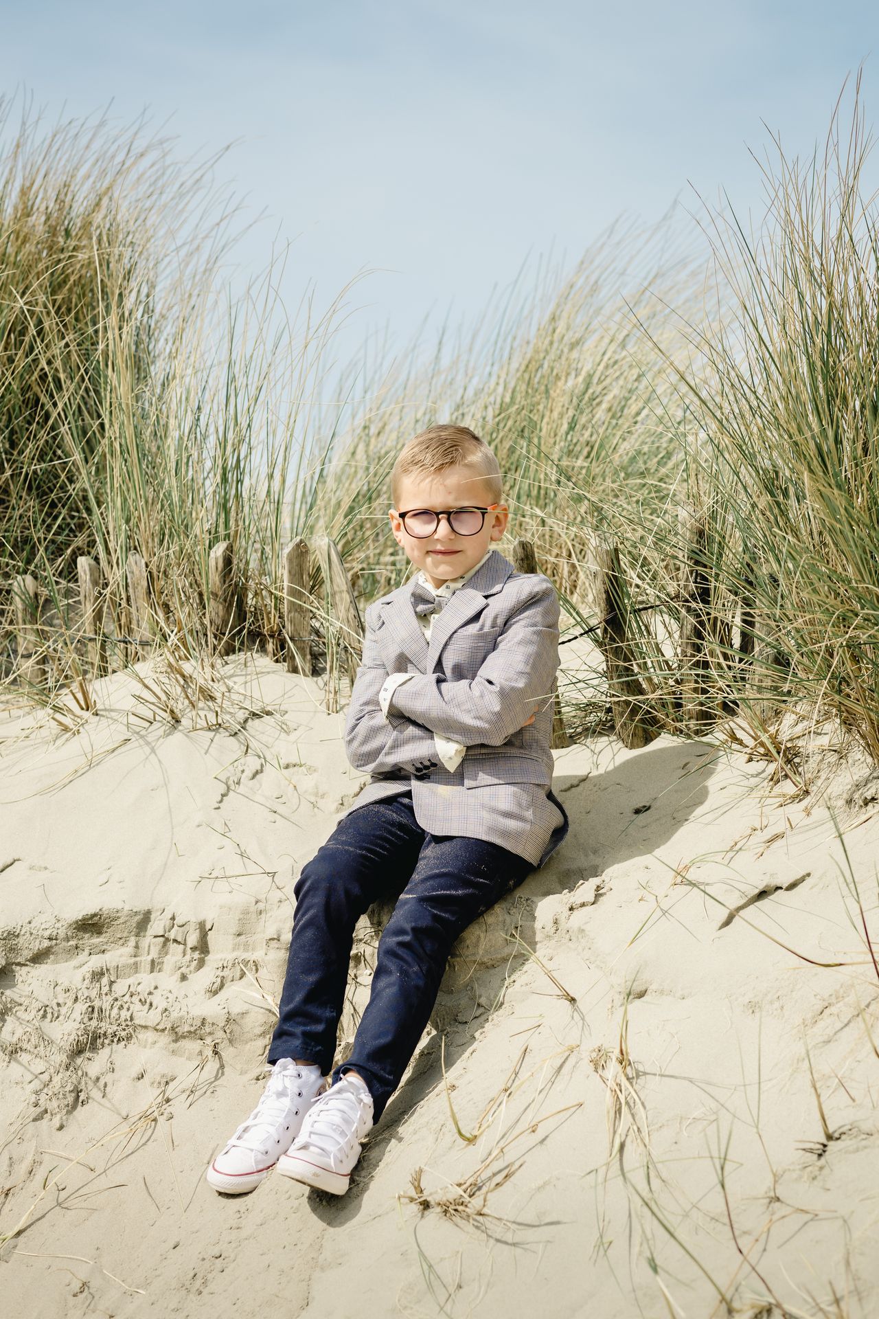 Lentefeest fotoshoot aan zee in Bredene met jongen in feestelijke outfit, zonnige dag en duinen op de achtergrond.