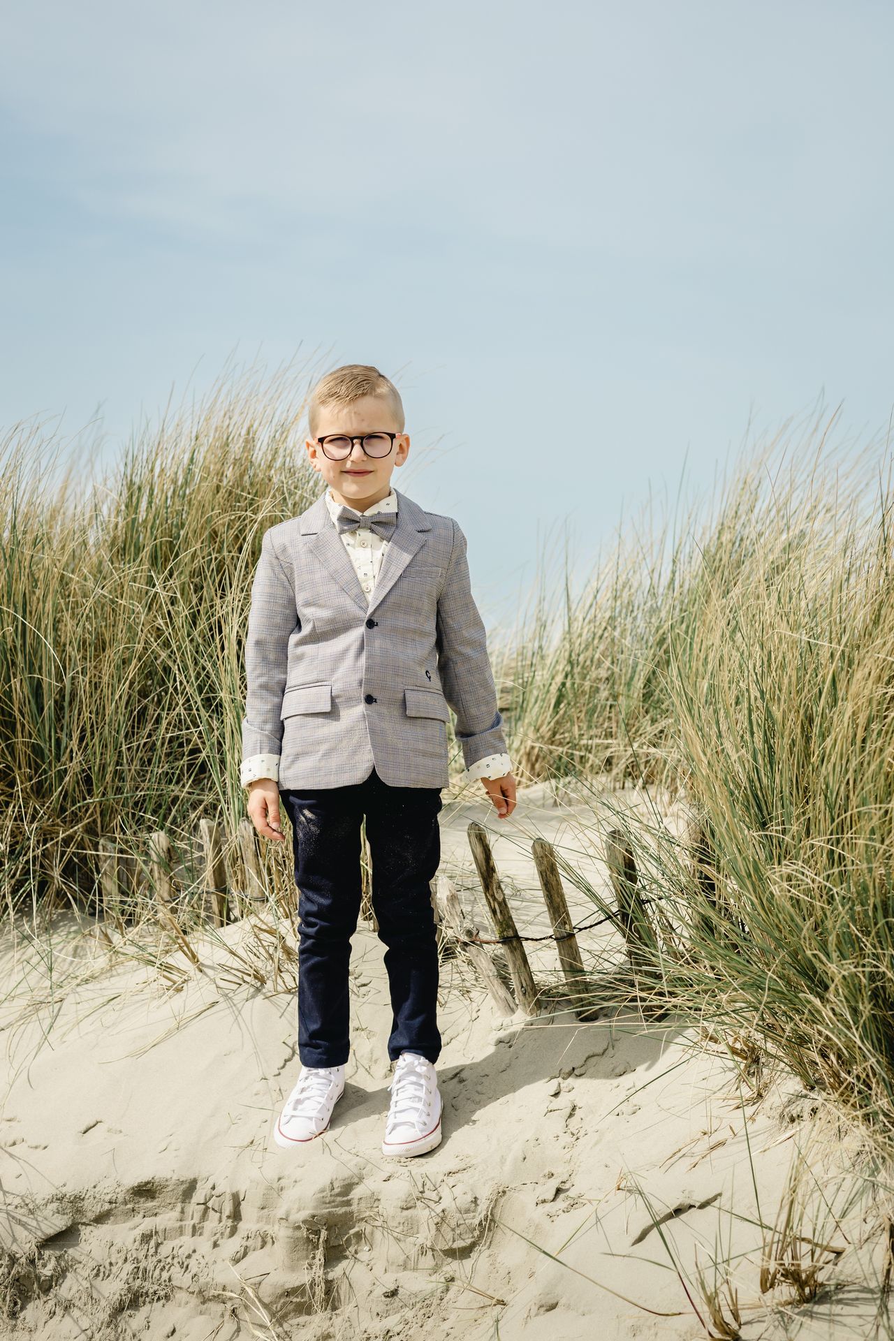 Fotoshoot voor lentefeest aan zee met stijlvolle outfit, duinen en bomen in zonnige setting.