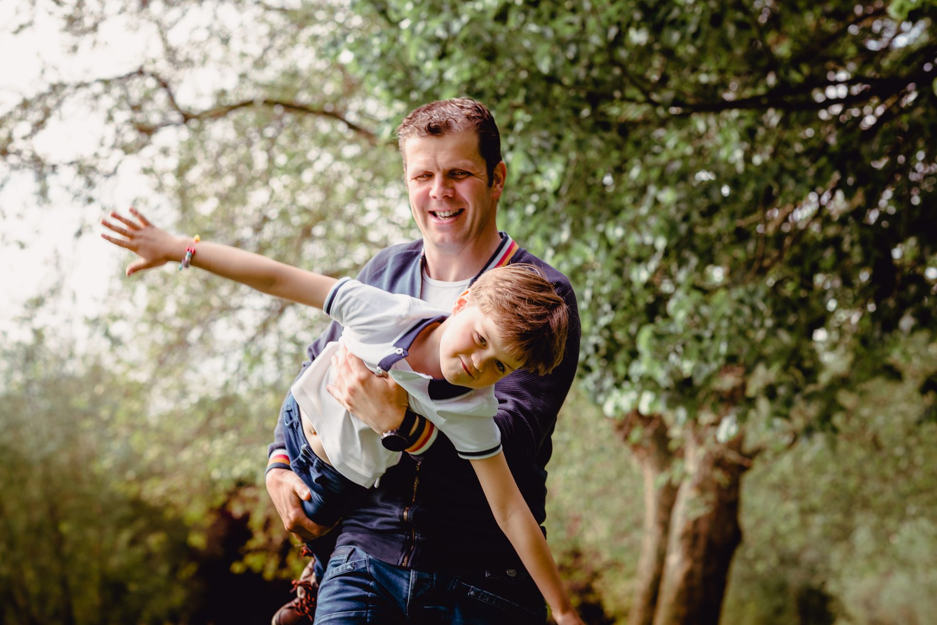 Fotoshoot van gezin in landelijke omgeving met zon en zachte wolken.