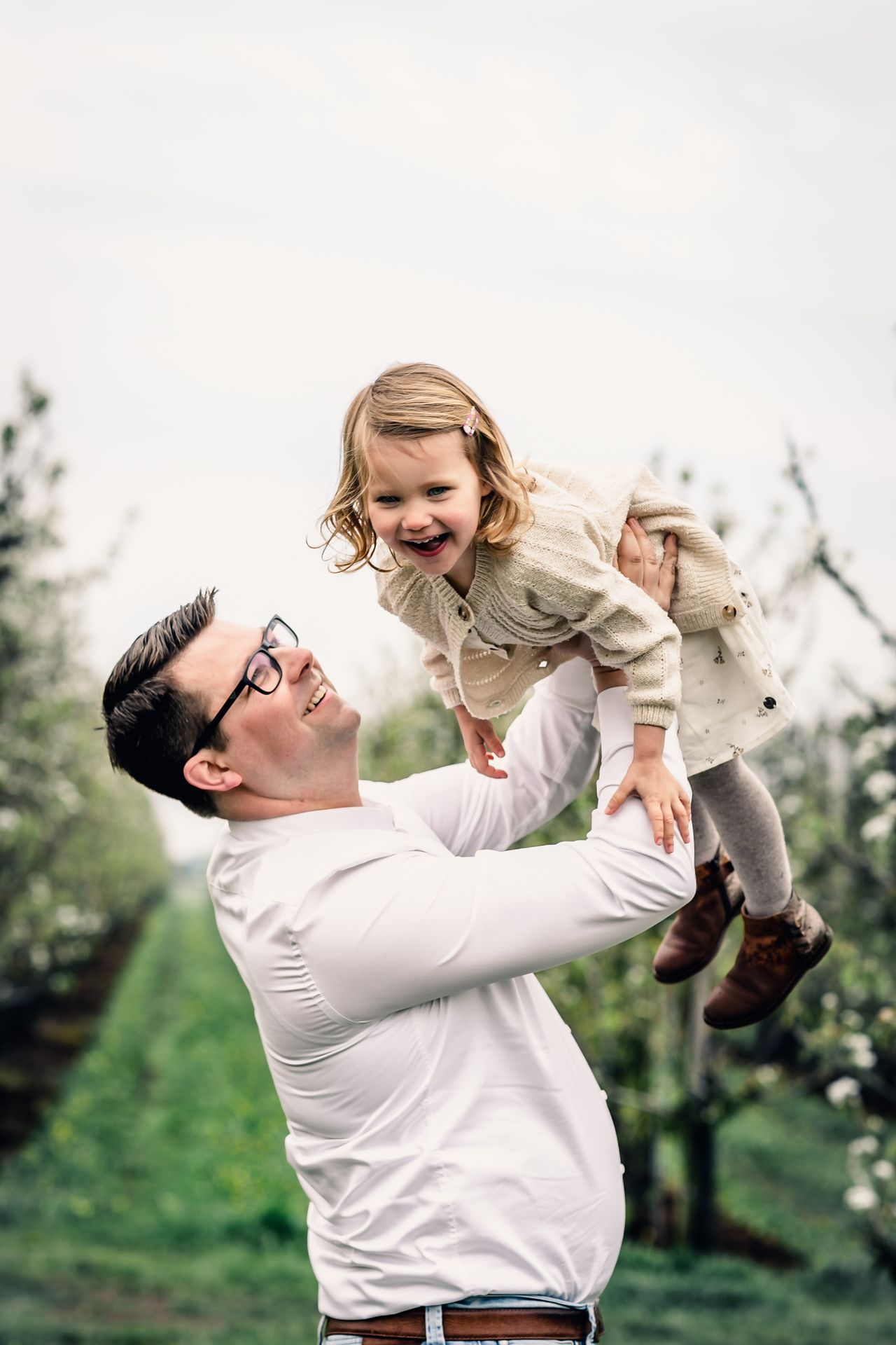 Gezinsmomenten vastgelegd tussen appelbloesems met zachte regen voor natuurlijke sfeer.