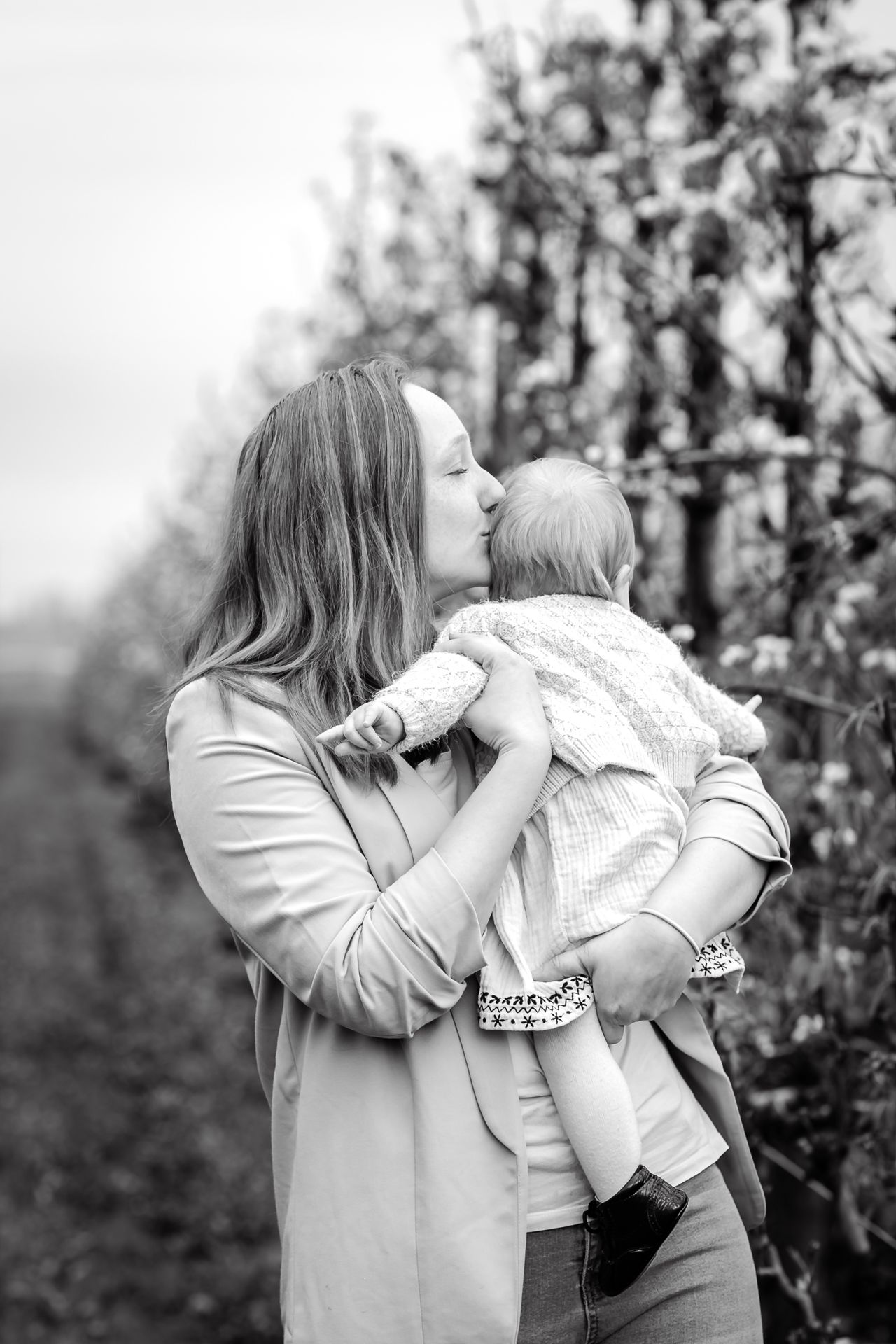 Familiefotoshoot in bloeiende appelboomgaard op regenachtige dag in België.