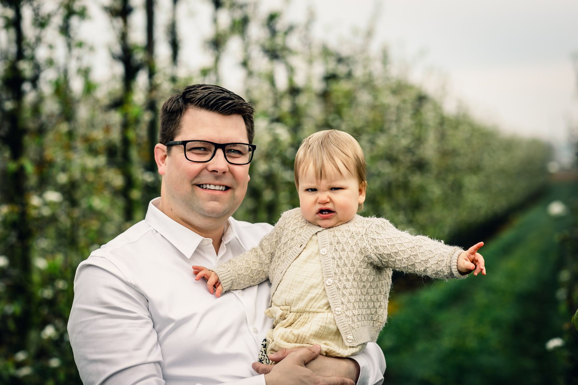 Familiefotoshoot in bloeiende appelboomgaard op regenachtige dag in België.