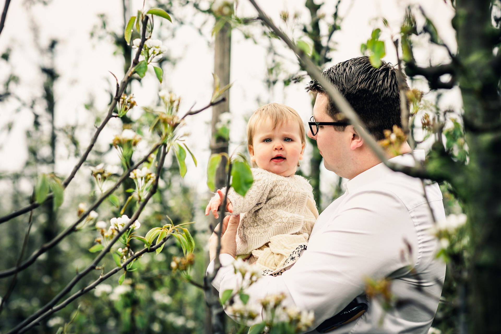 Familiefotoshoot in bloeiende appelboomgaard op regenachtige dag in België.