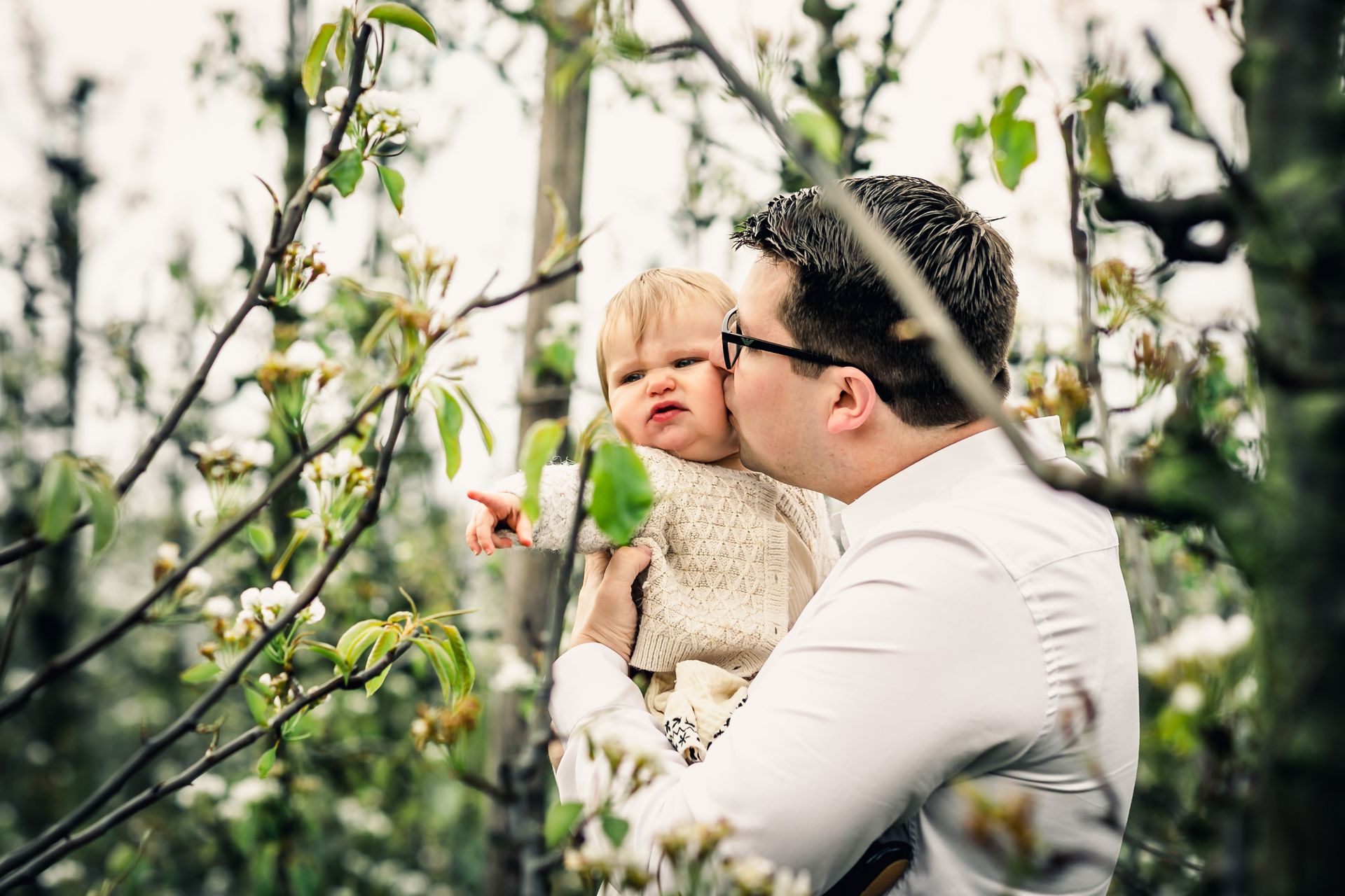 Romantische familiefoto’s in appelboomgaard met bloesems en speelse regendruppels.