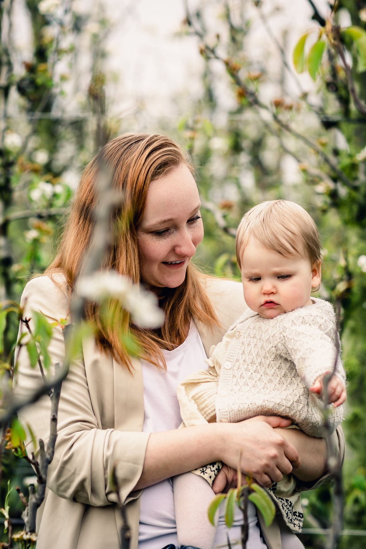 Romantische familiefoto’s in appelboomgaard met bloesems en speelse regendruppels.