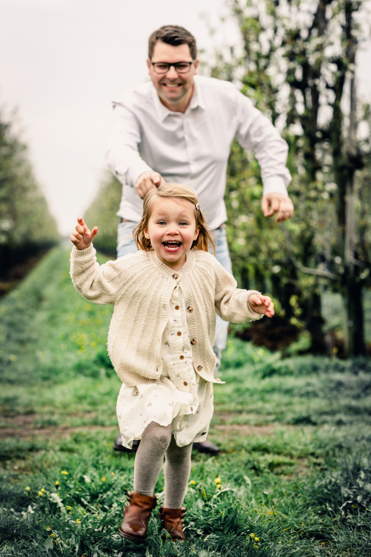 Romantische familiefoto’s in appelboomgaard met bloesems en speelse regendruppels.
