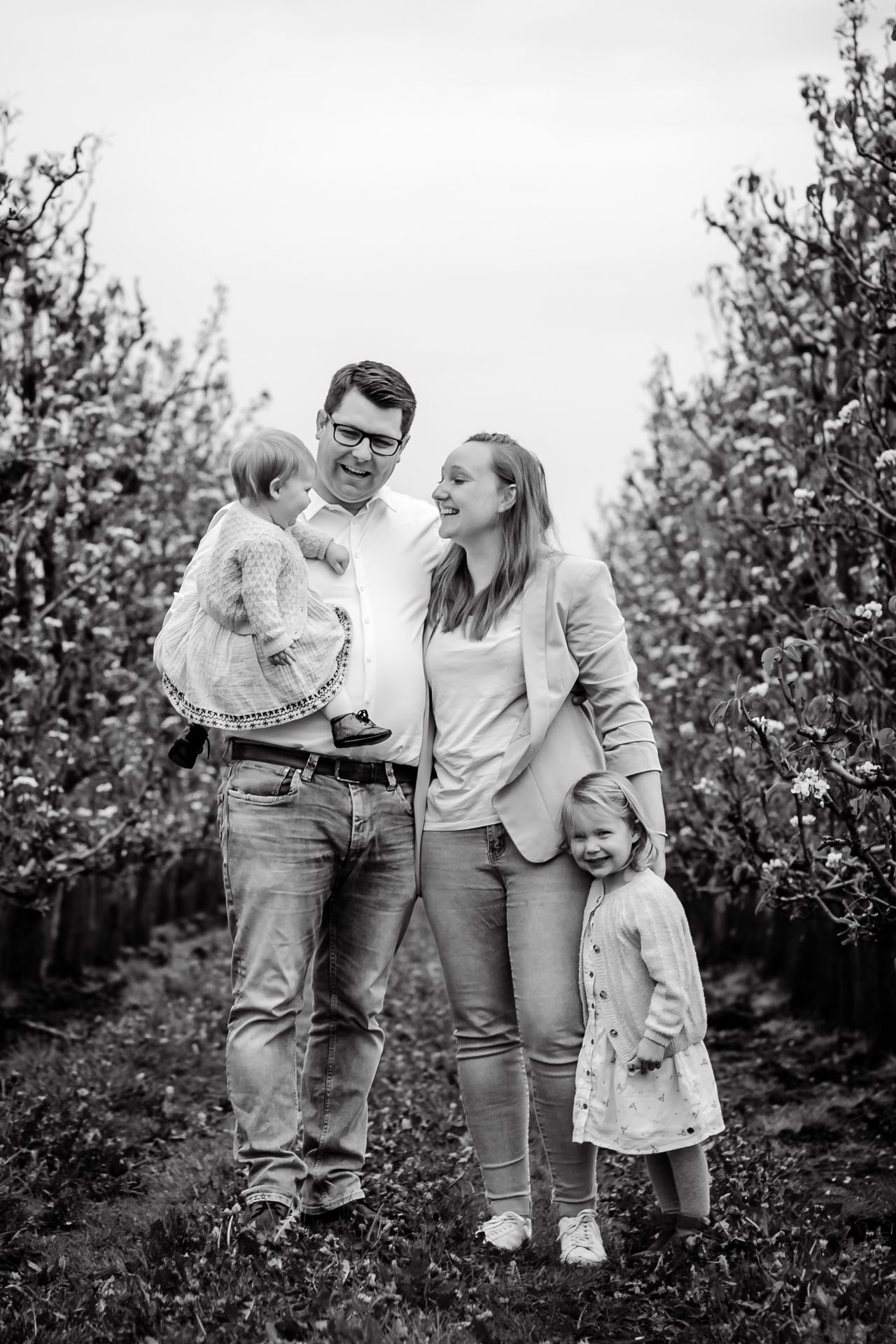 Tijdloze familiefotografie in appelboomgaard met bloesems en lichte regenbuien