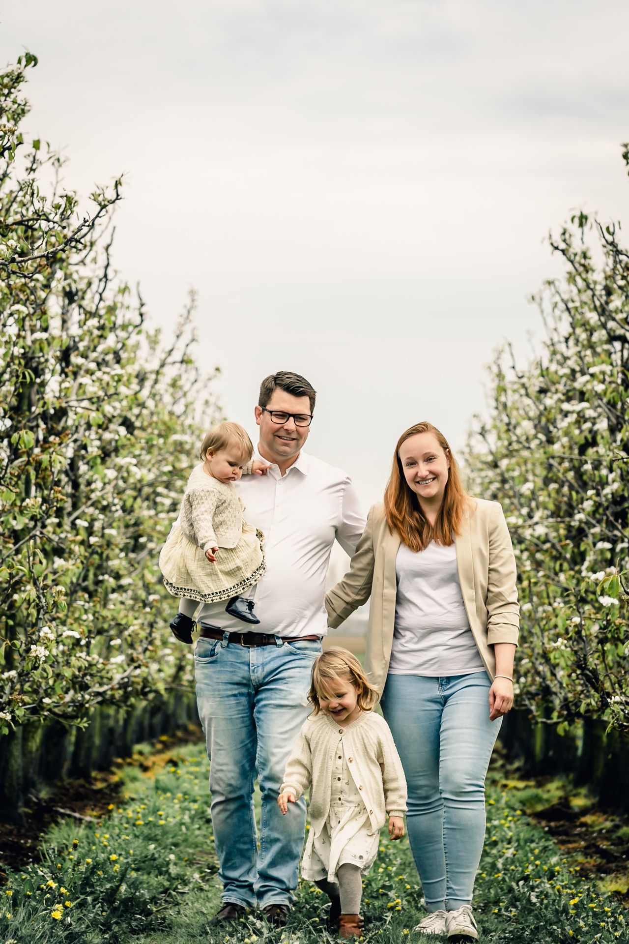 Tijdloze familiefotografie in appelboomgaard met bloesems en lichte regenbuien