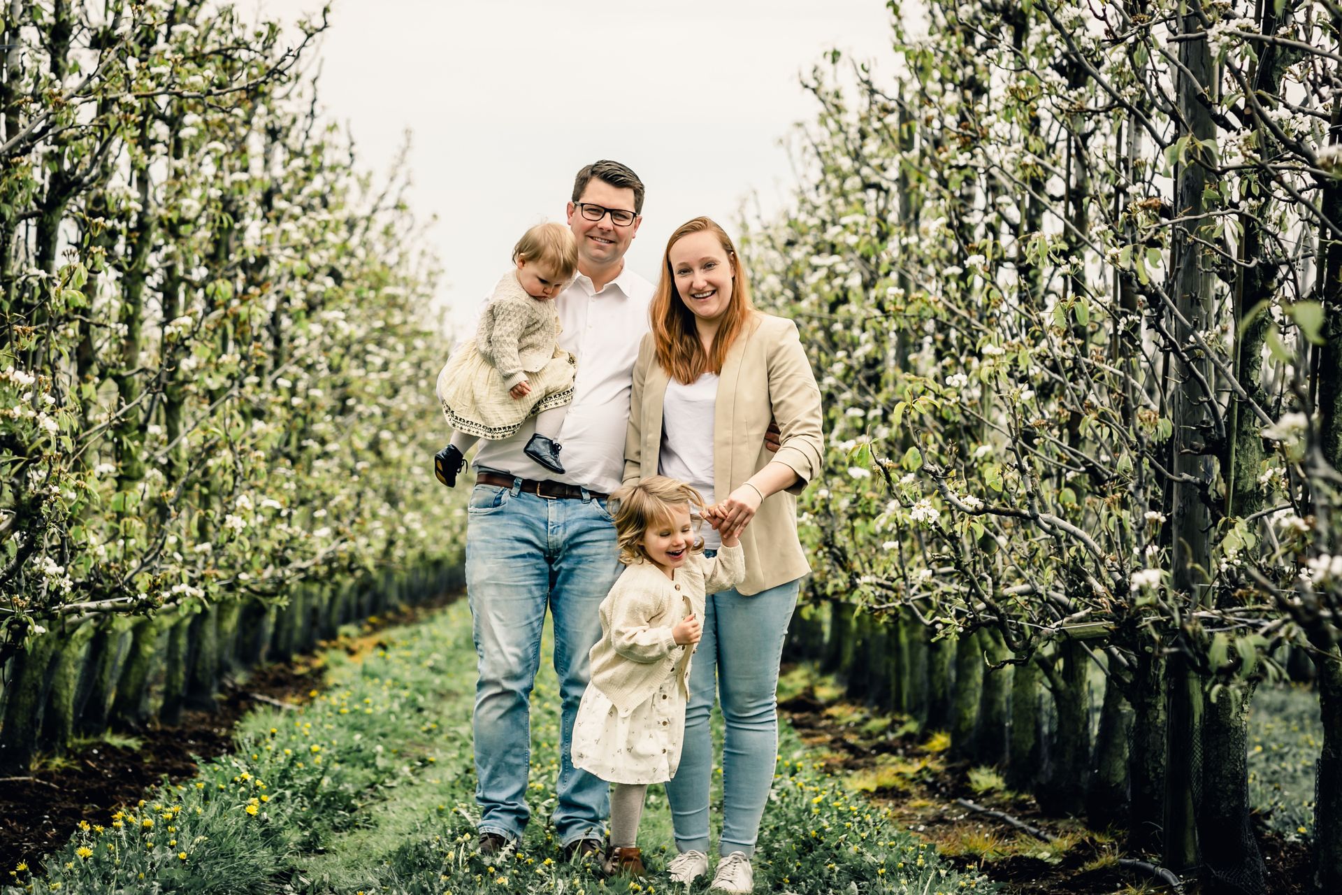 Romantische familiefoto’s in appelboomgaard met bloesems en speelse regendruppels.